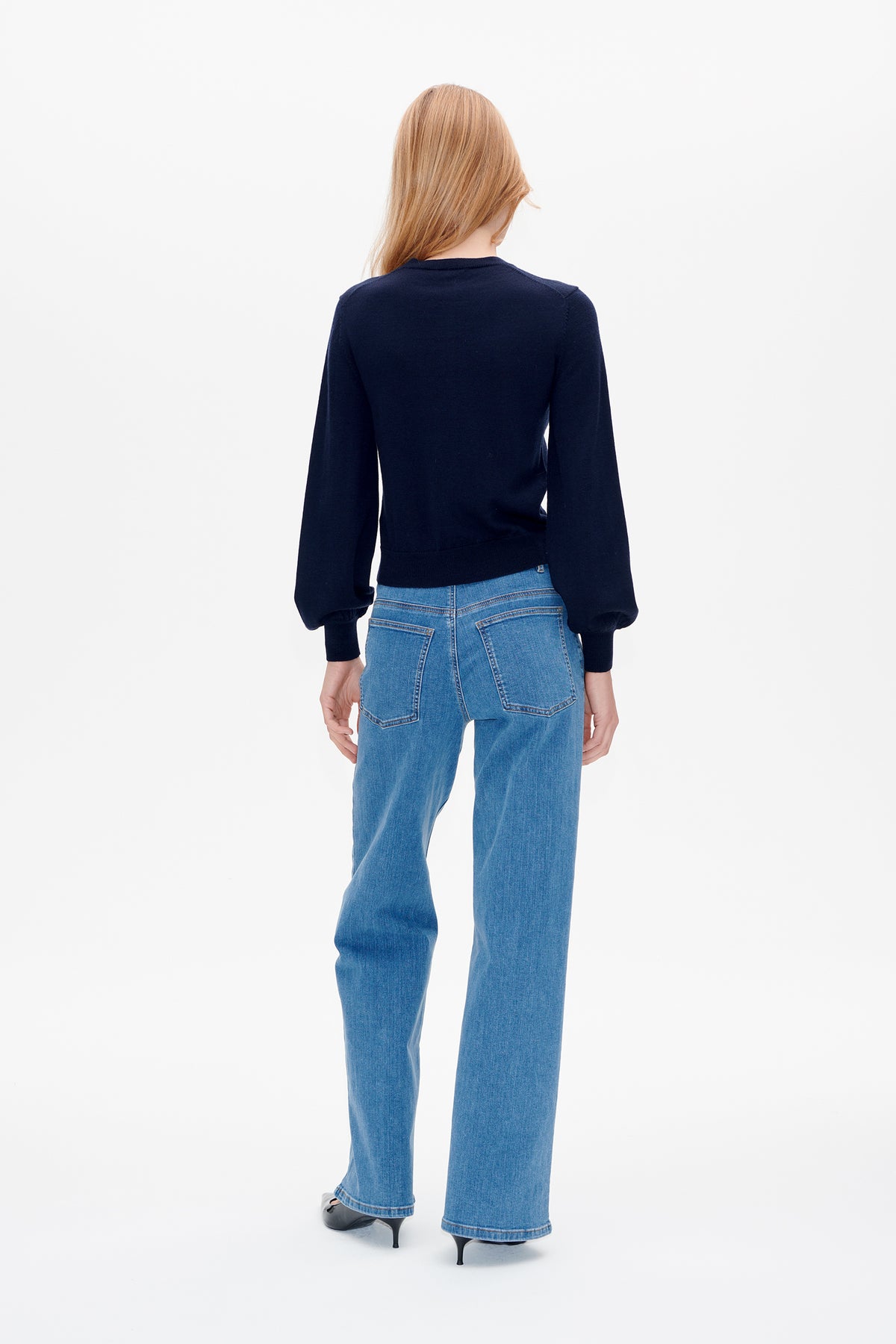 Back view of a model wearing a dark navy knit sweater with voluminous sleeves and light blue wide-leg jeans.
