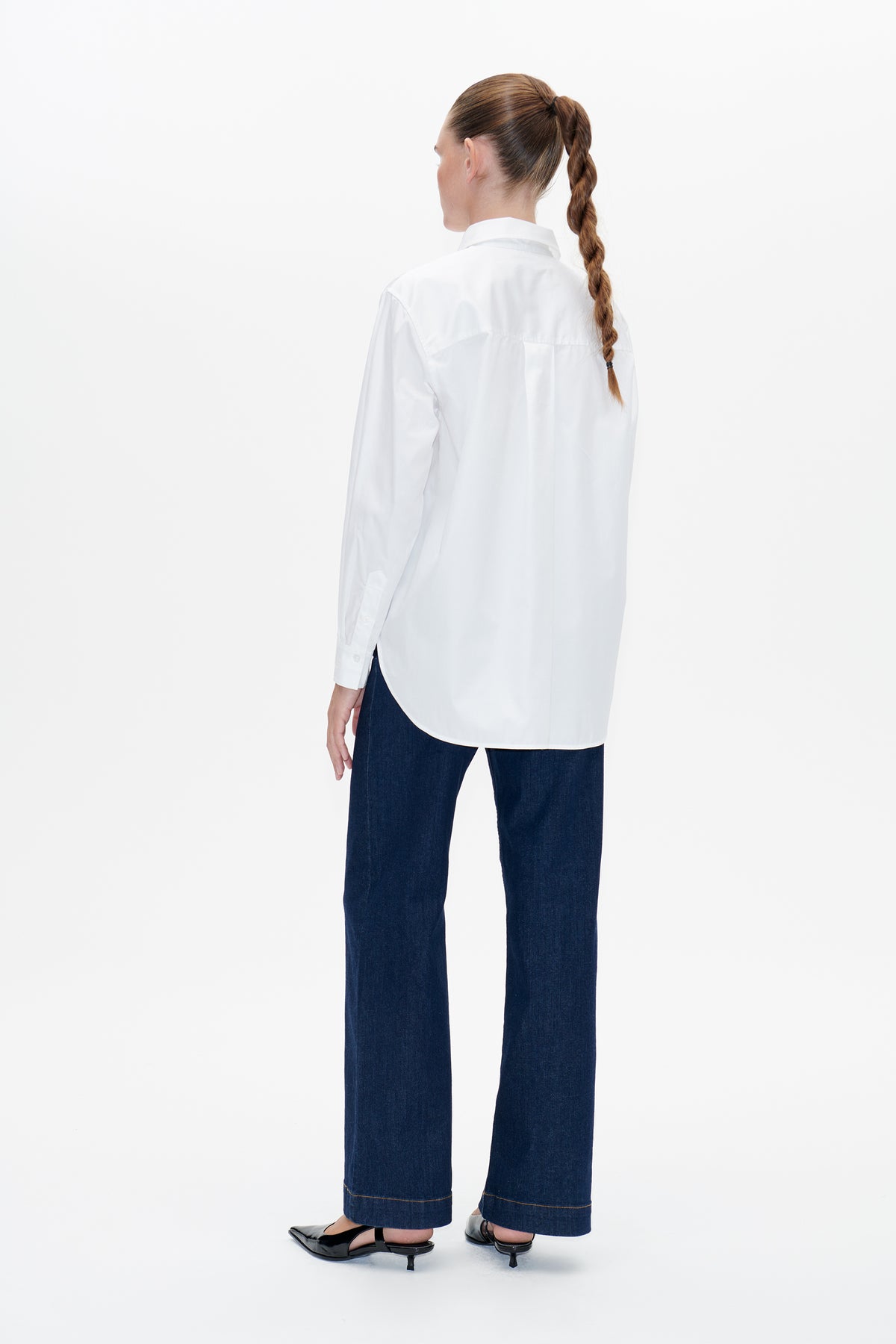 Back view of a white long-sleeved shirt with a pointed collar, shoulder yoke and curved hem, worn with dark jeans.