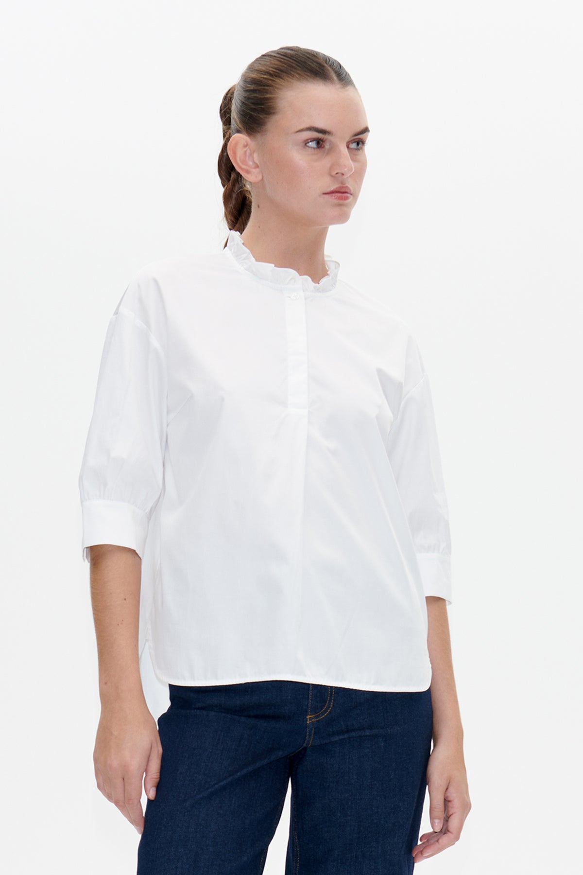 Front view of a white blouse with a ruffled stand collar, button placket and short gathered sleeves, styled with dark blue jeans.