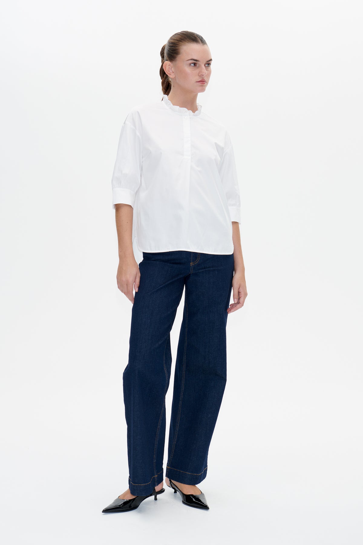 Model wearing a white blouse with a ruffled collar and three-quarter sleeves, paired with dark blue jeans.