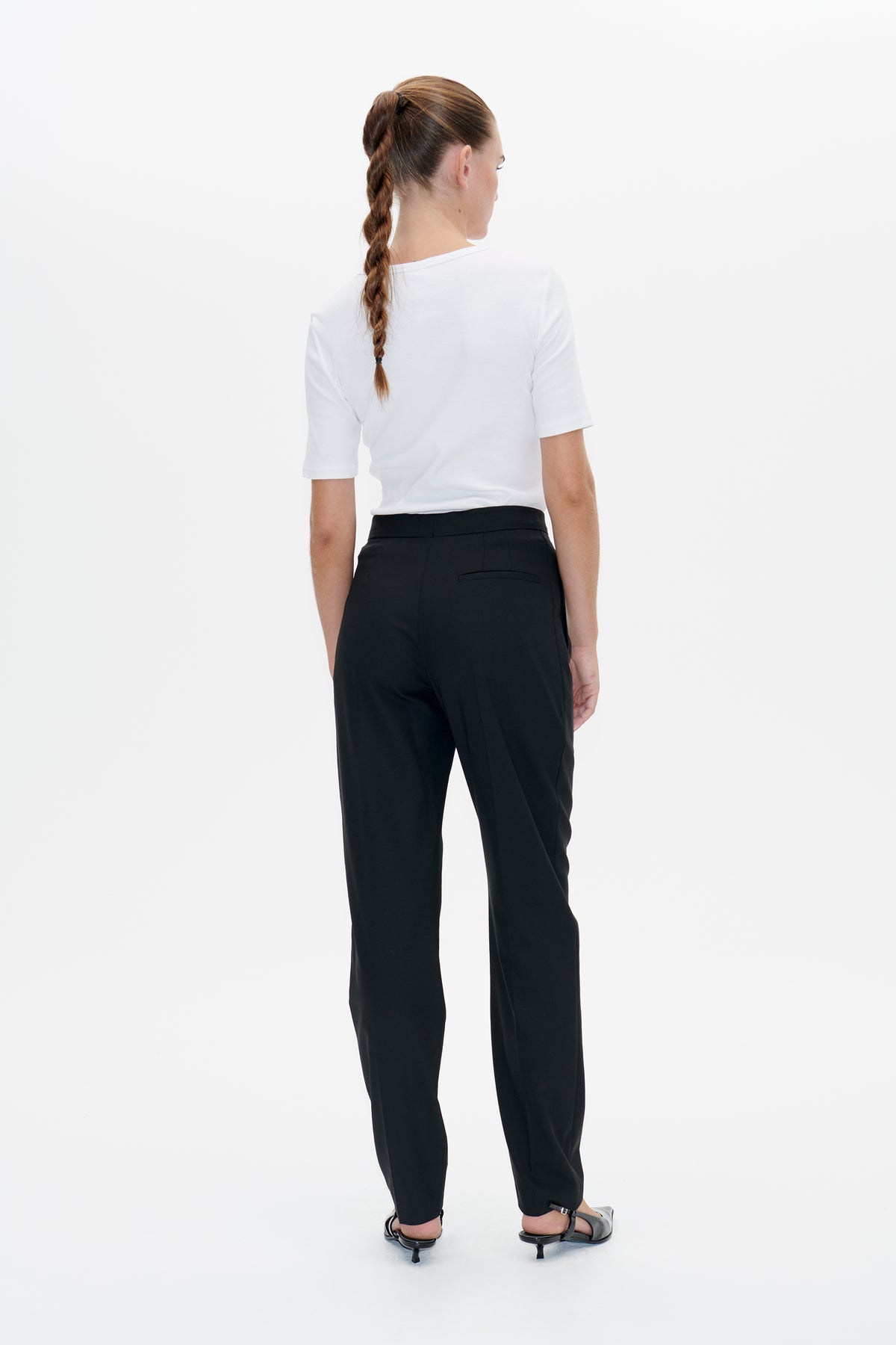 Back view of a model wearing a plain white short-sleeved top and black tailored trousers with a rear welt pocket.