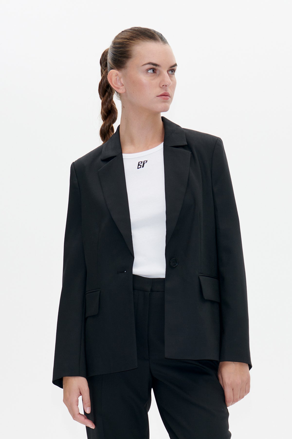 Model wearing a black single-button blazer over a white ribbed top with a small BP logo and black trousers.