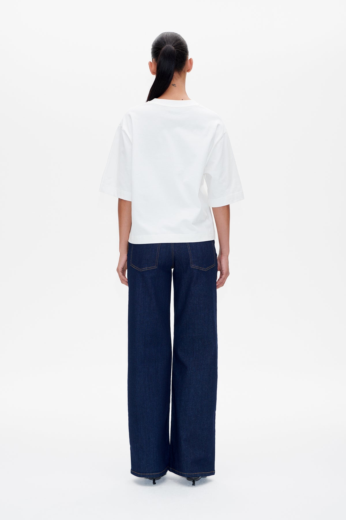 Back view of a model wearing a plain white short-sleeved T-shirt with dark blue wide-leg jeans.