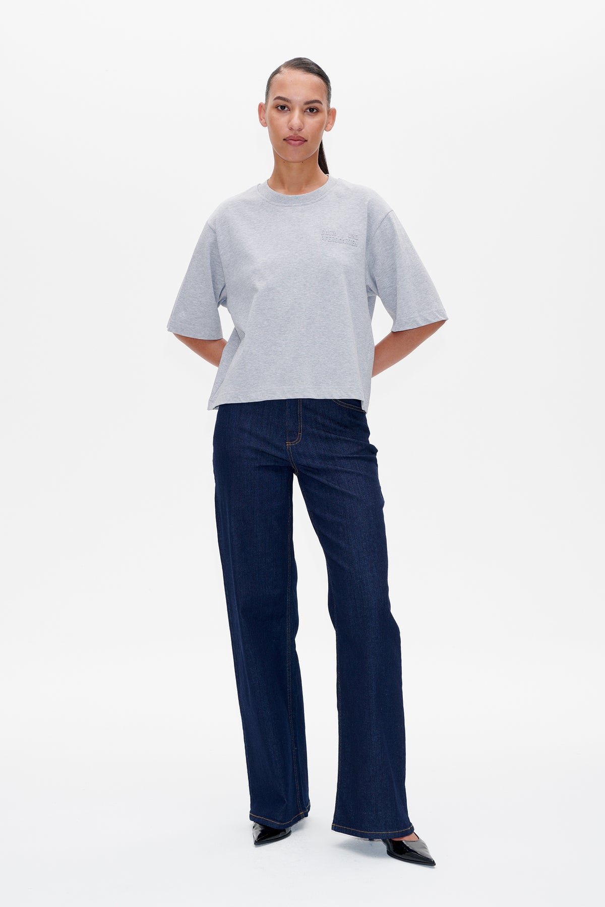Model wearing a light grey oversized short-sleeve T-shirt with subtle chest lettering and dark blue wide-leg jeans, front view.