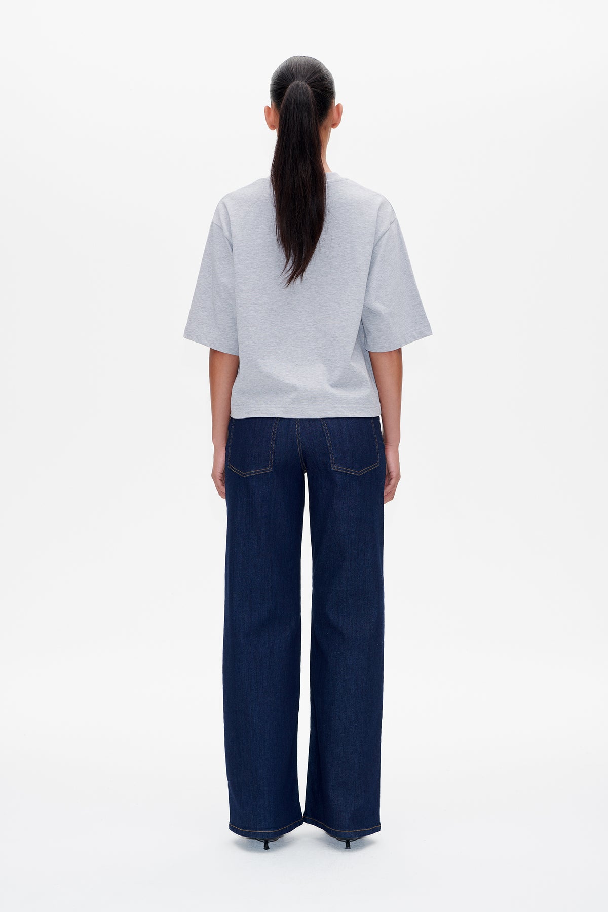 Back view of a model wearing a plain light grey short-sleeved T-shirt and dark indigo wide-leg jeans.
