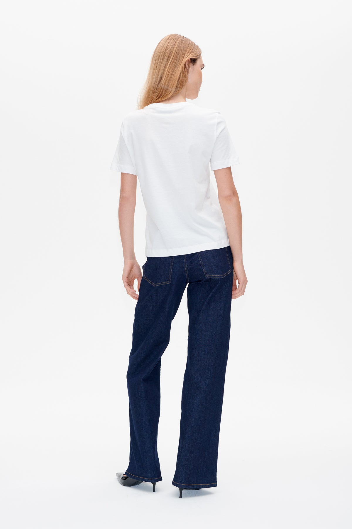 Back view of a model wearing a plain white short-sleeved T-shirt with dark blue wide-leg jeans.