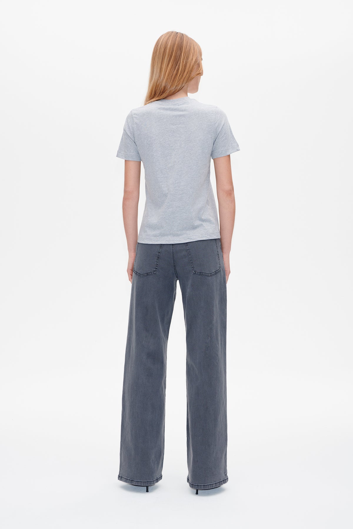 Back view of a model wearing a plain light grey short-sleeved T-shirt with wide-leg dark grey jeans.