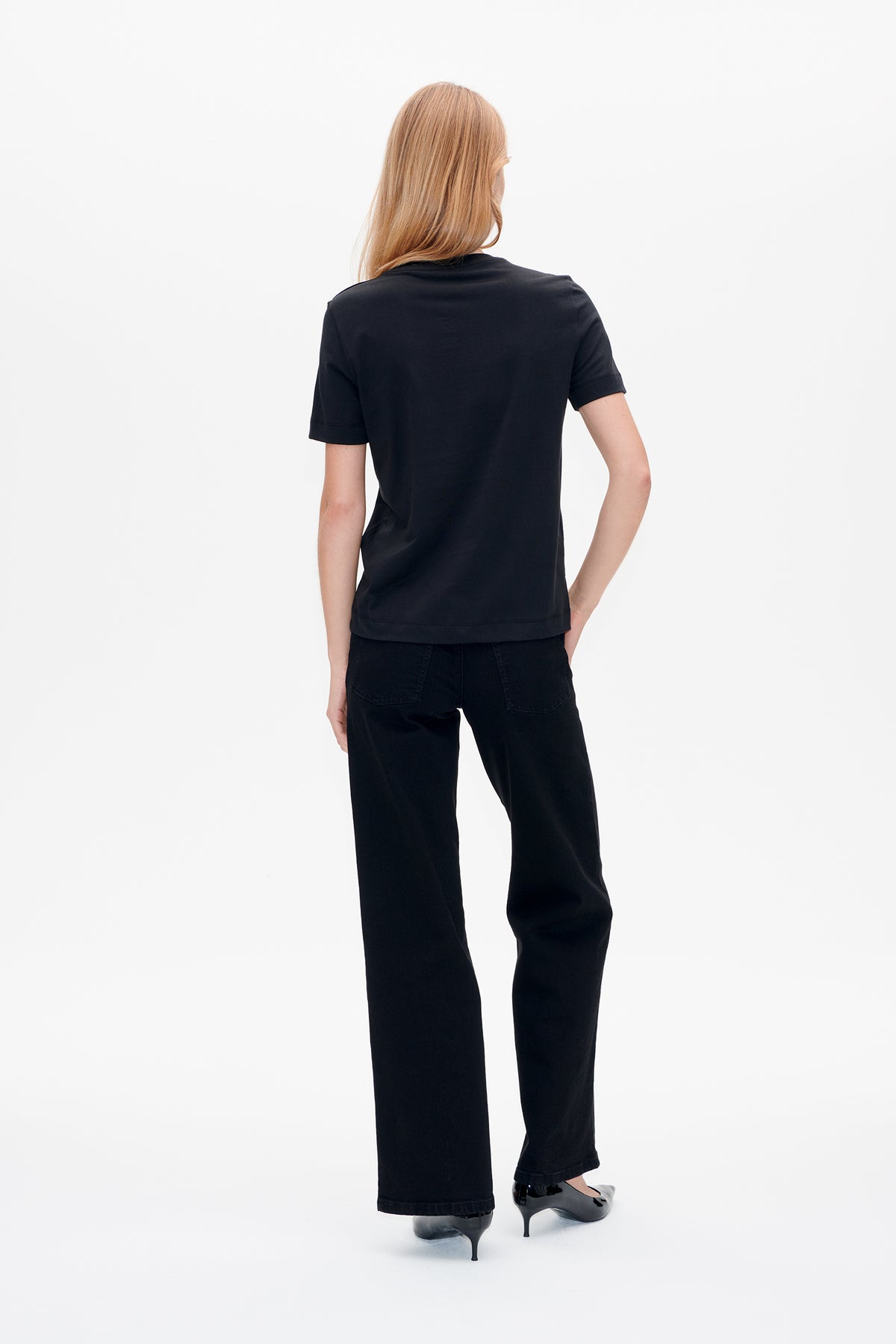 Back view of a plain black short-sleeved T-shirt worn with black wide-leg jeans.