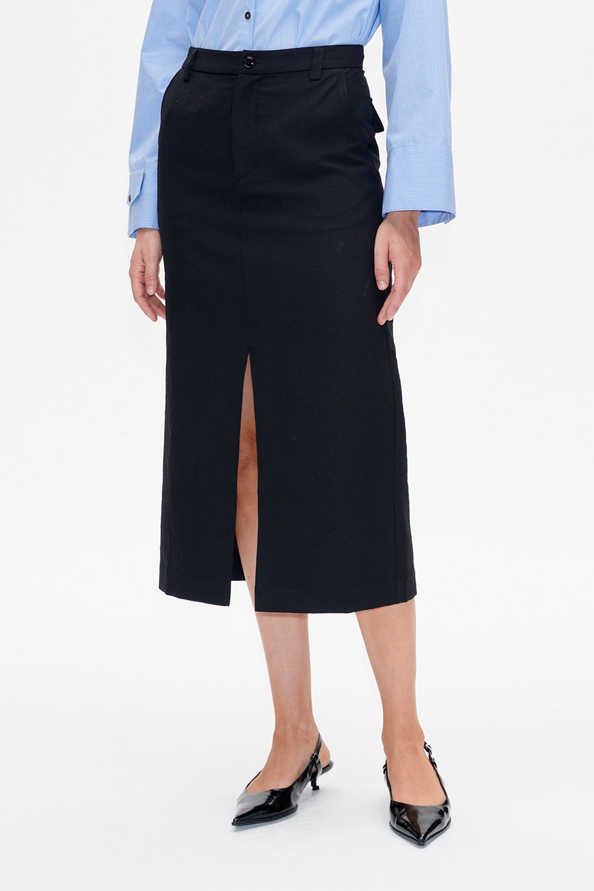 Front view of a black high-waisted midi skirt with belt loops and a long front slit, styled with a blue pinstriped shirt.