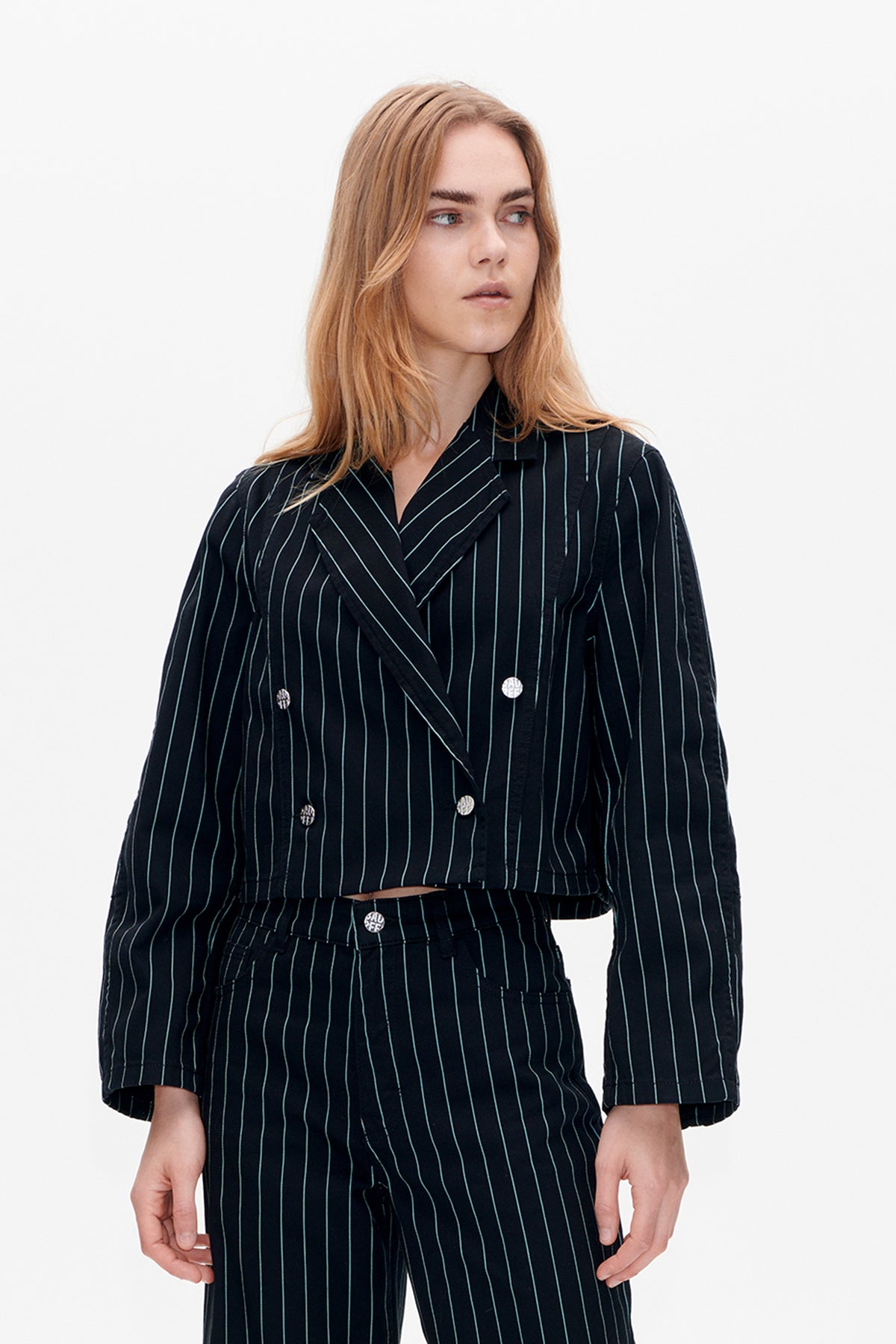 Front view of a model wearing a dark cropped double-breasted jacket and matching trousers with thin pale wavy stripes and silver buttons.