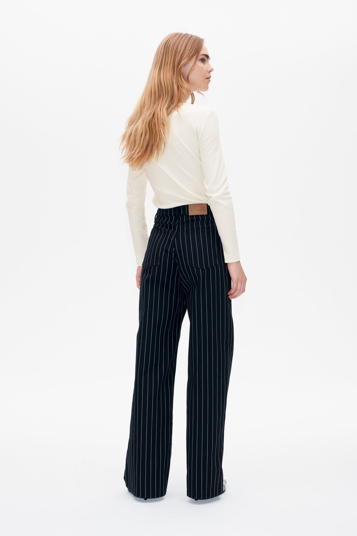 Model shown from behind in a cream long-sleeve top and black pinstripe wide-leg trousers with rear patch pockets.