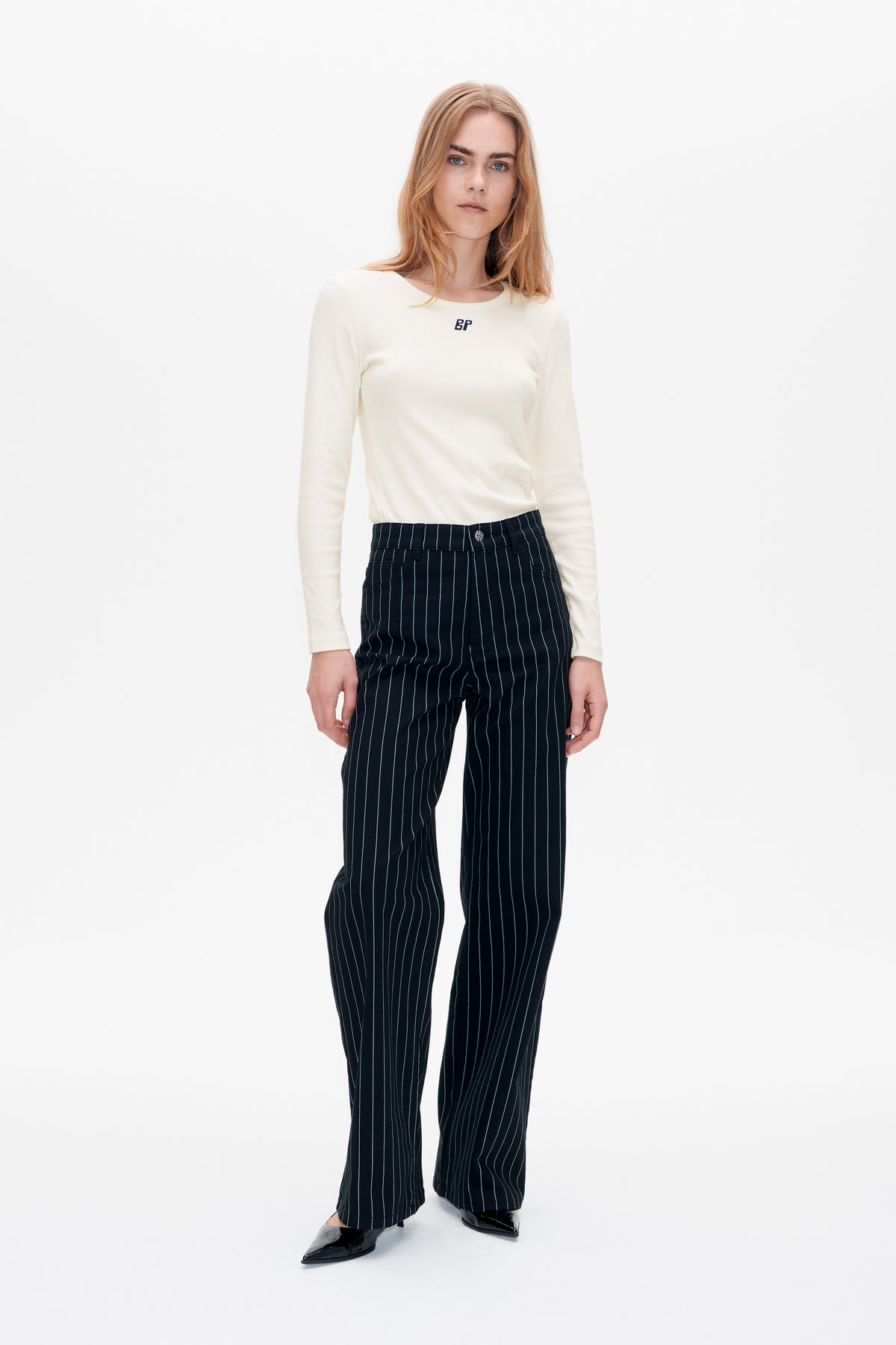 Front-facing studio look featuring an ivory long-sleeve top with a small chest logo and navy wide-leg trousers with fine vertical stripes.