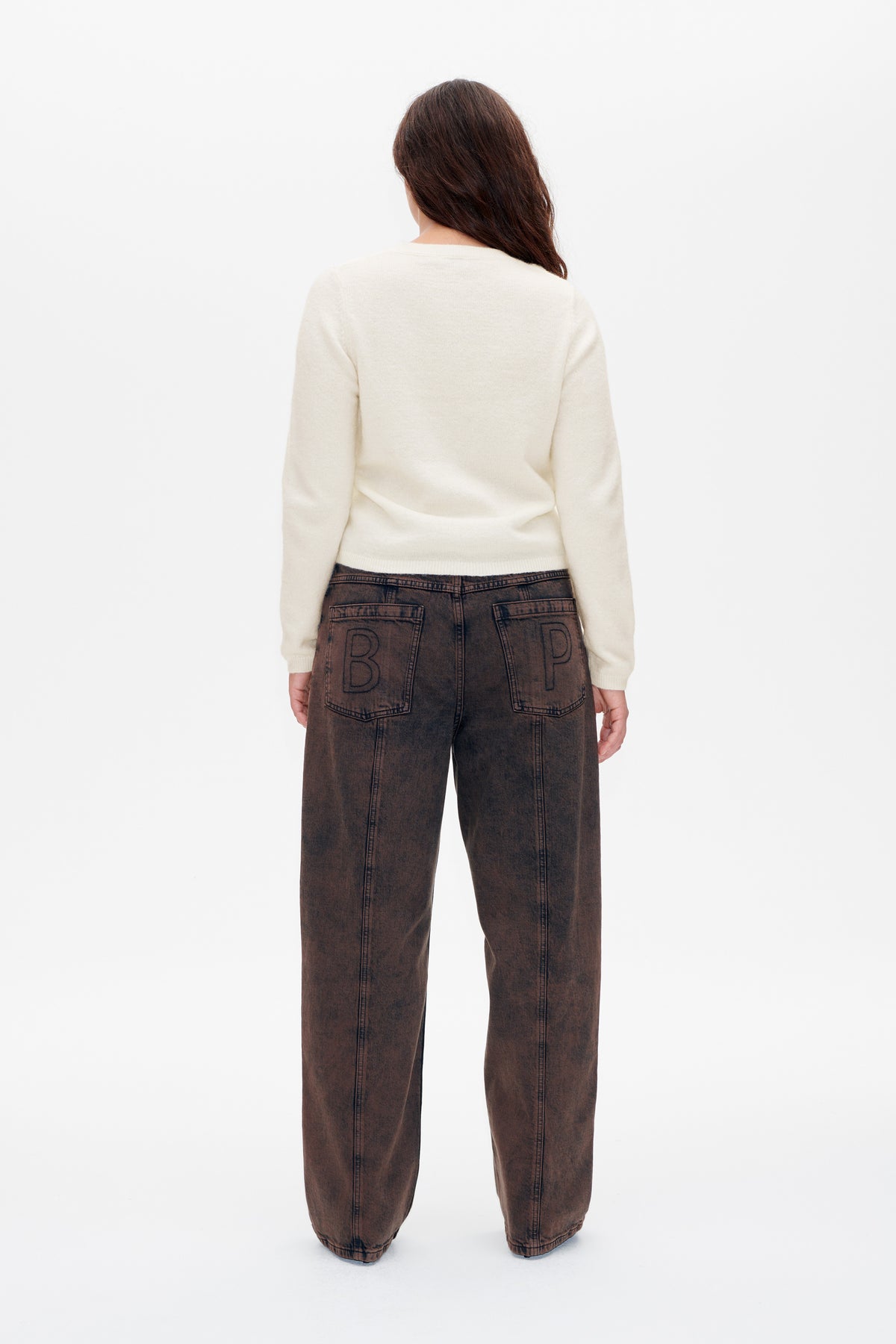 Rückenansicht eines Models, das einen elfenbeinfarbenen Strickpullover und weit geschnittene, gewaschene braune Jeans trägt, mit konturierter Schrift auf den Gesäßtaschen.