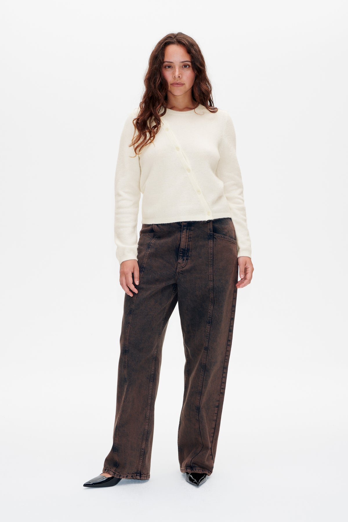Vorderansicht eines Models, das eine elfenbeinfarbene Strickjacke mit durchgehender Knopfleiste und dunkelbraun gewaschene, weit geschnittene Jeans trägt.