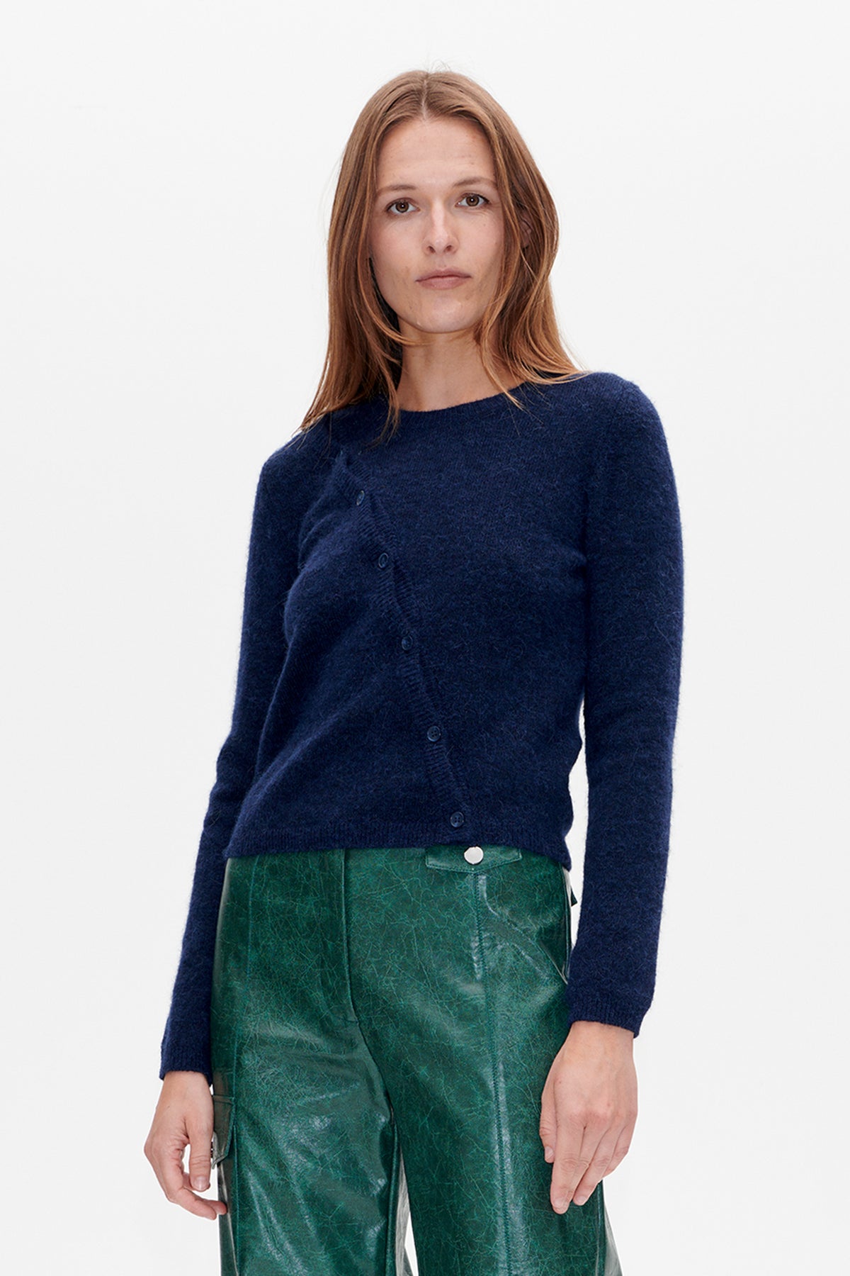 Front view of a model wearing a navy button-front knit cardigan with shiny textured green trousers