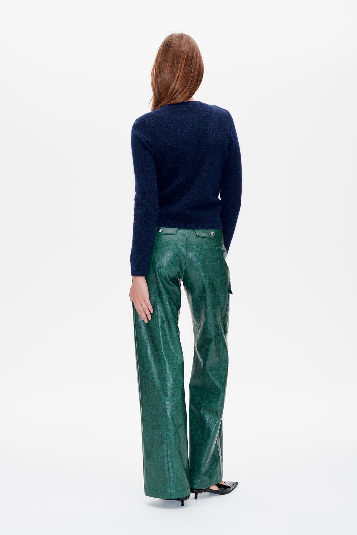 Achteraanzicht van een model dat een marineblauwe gebreide trui met lange mouwen en een groene, glanzende broek met wijde pijpen draagt.