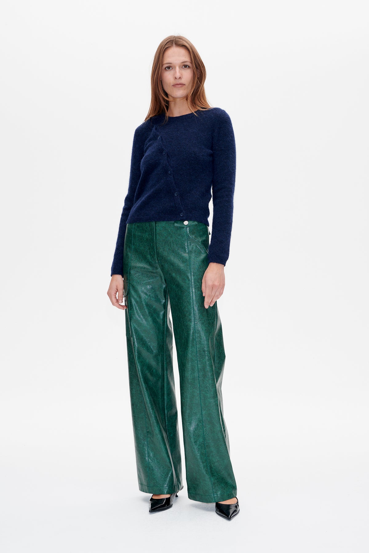 Vooraanzicht van een model met een marineblauwe gebreide cardigan met knoopsluiting aan de voorkant en een wijde groene broek met een glanzende, gemêleerde afwerking.
