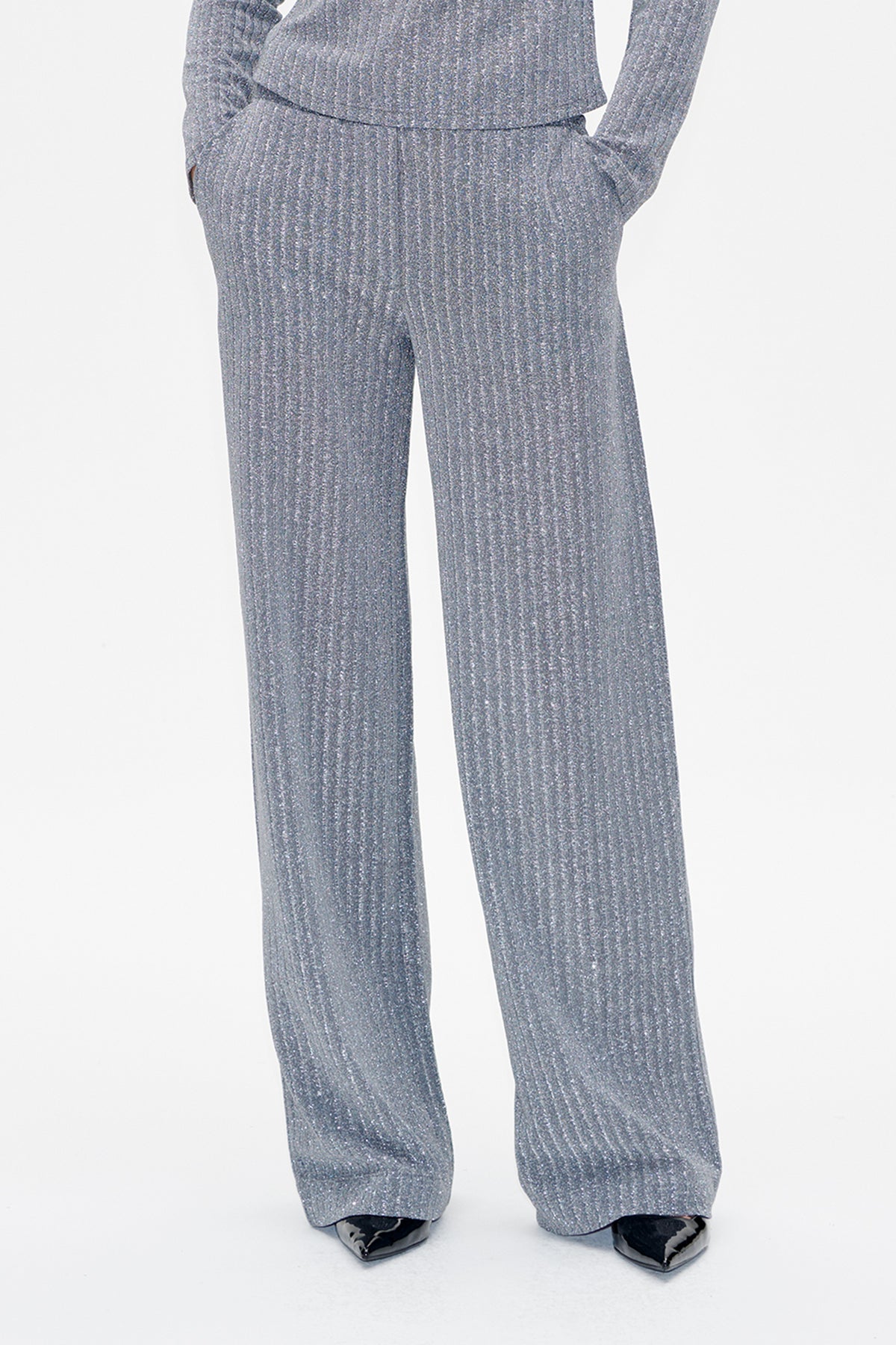 Front detail of shimmering grey straight-leg trousers with side pockets and long hems over black pointed shoes.