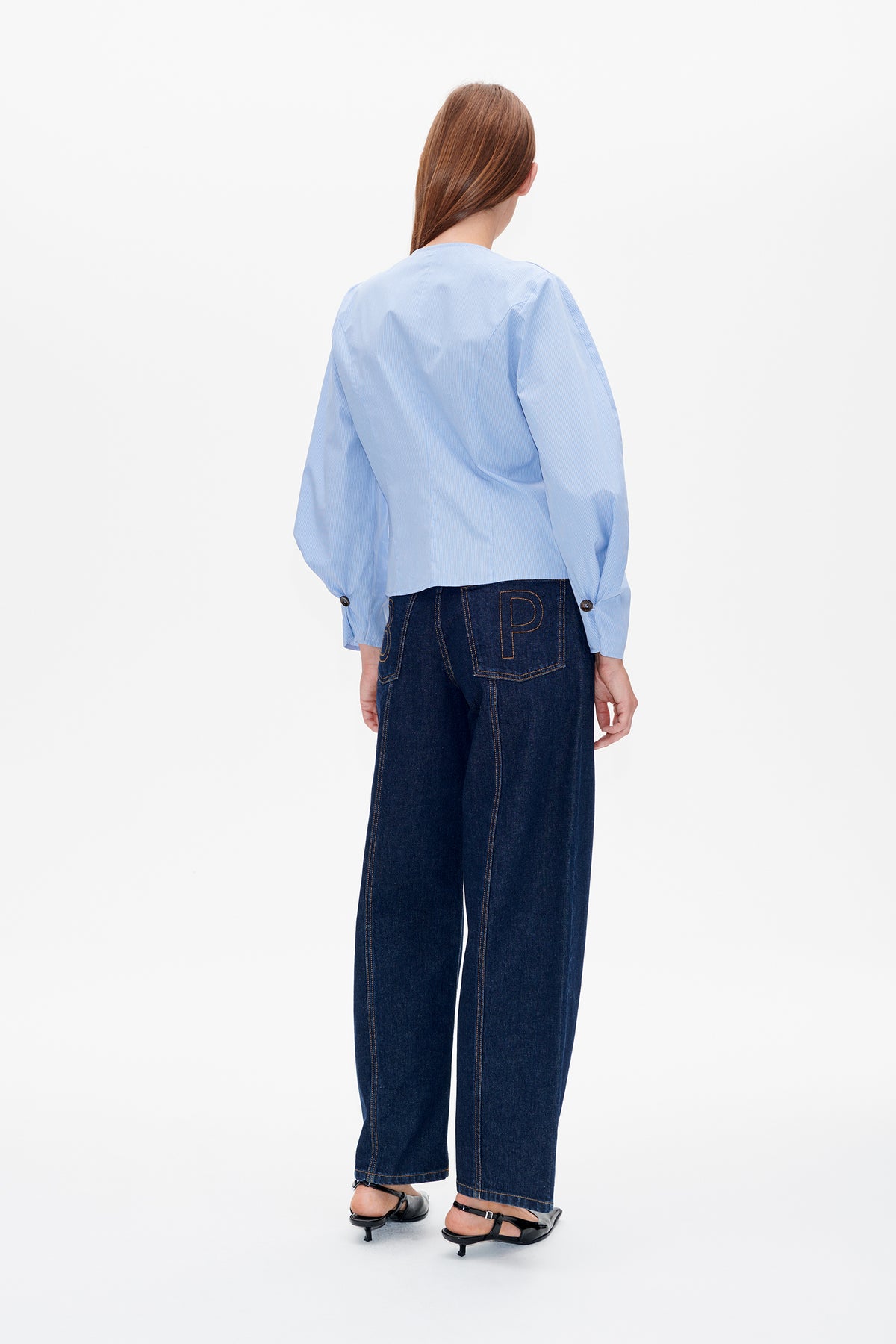 Back view of a light blue pinstriped blouse with voluminous sleeves, paired with dark wide-leg jeans featuring outlined back pockets.
