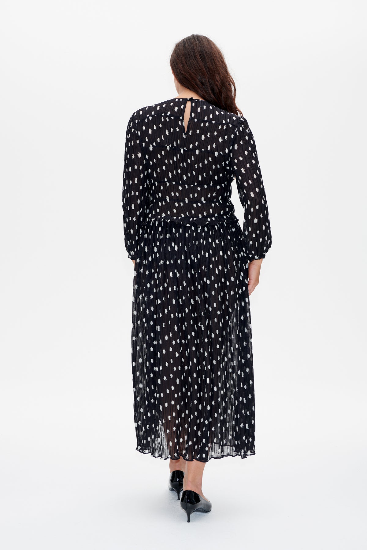 Back view of a long-sleeved black dress with an irregular white dot pattern, gathered waist, pleated skirt and keyhole closure.