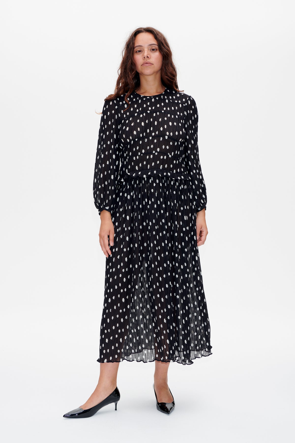 Front view of a black long-sleeved midi dress with an irregular white dot pattern, pleated texture and ruffled waist seam.