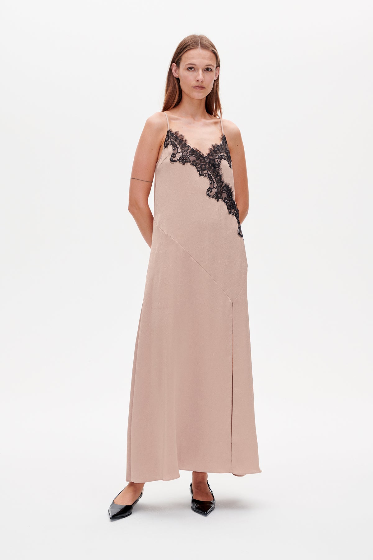 Front view of a blush-pink slip dress with thin straps, diagonal seams and black lace trim across the V-neckline.