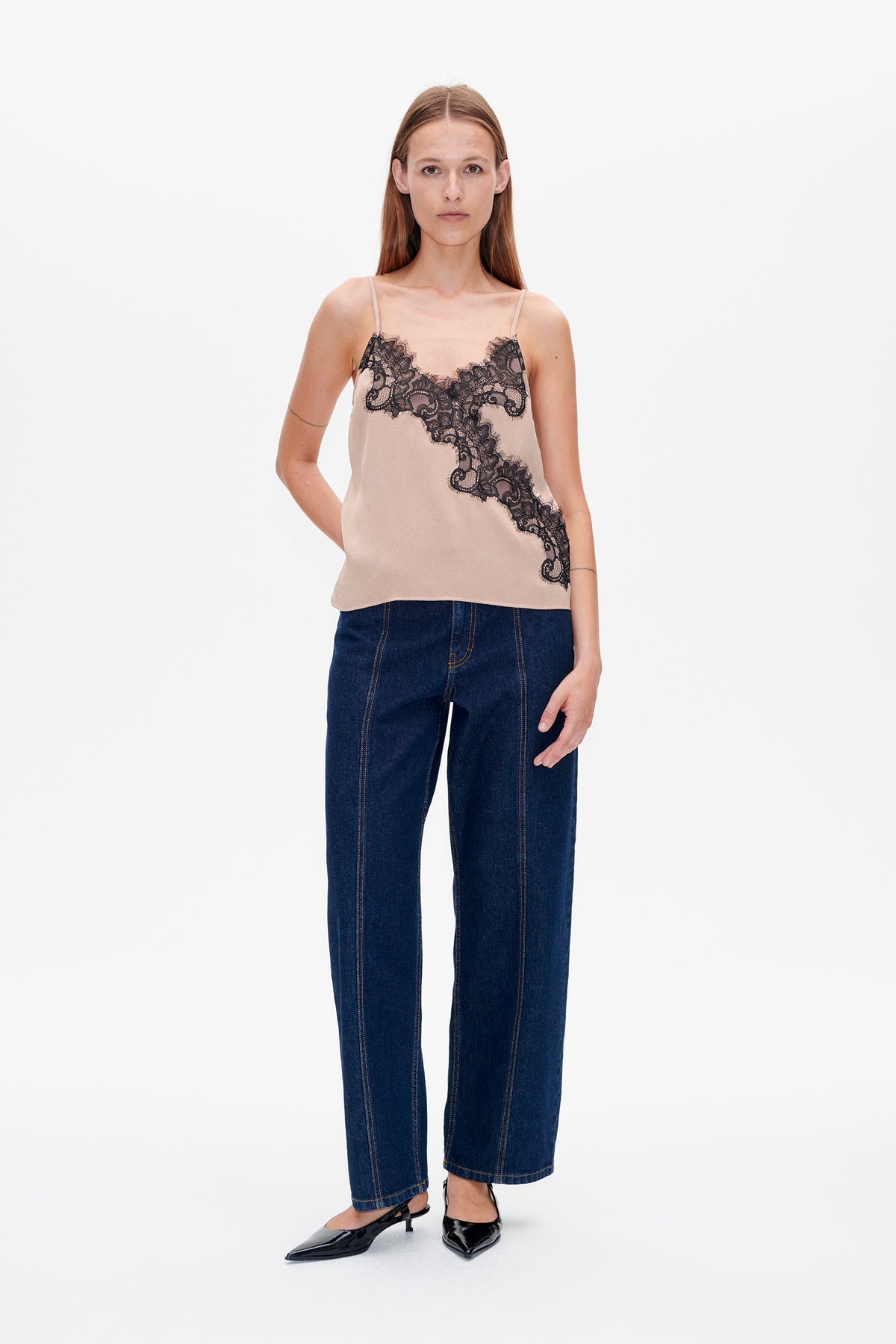 Vooraanzicht van een model dat een lichtroze topje met zwarte kant en donkerblauwe jeans draagt.
