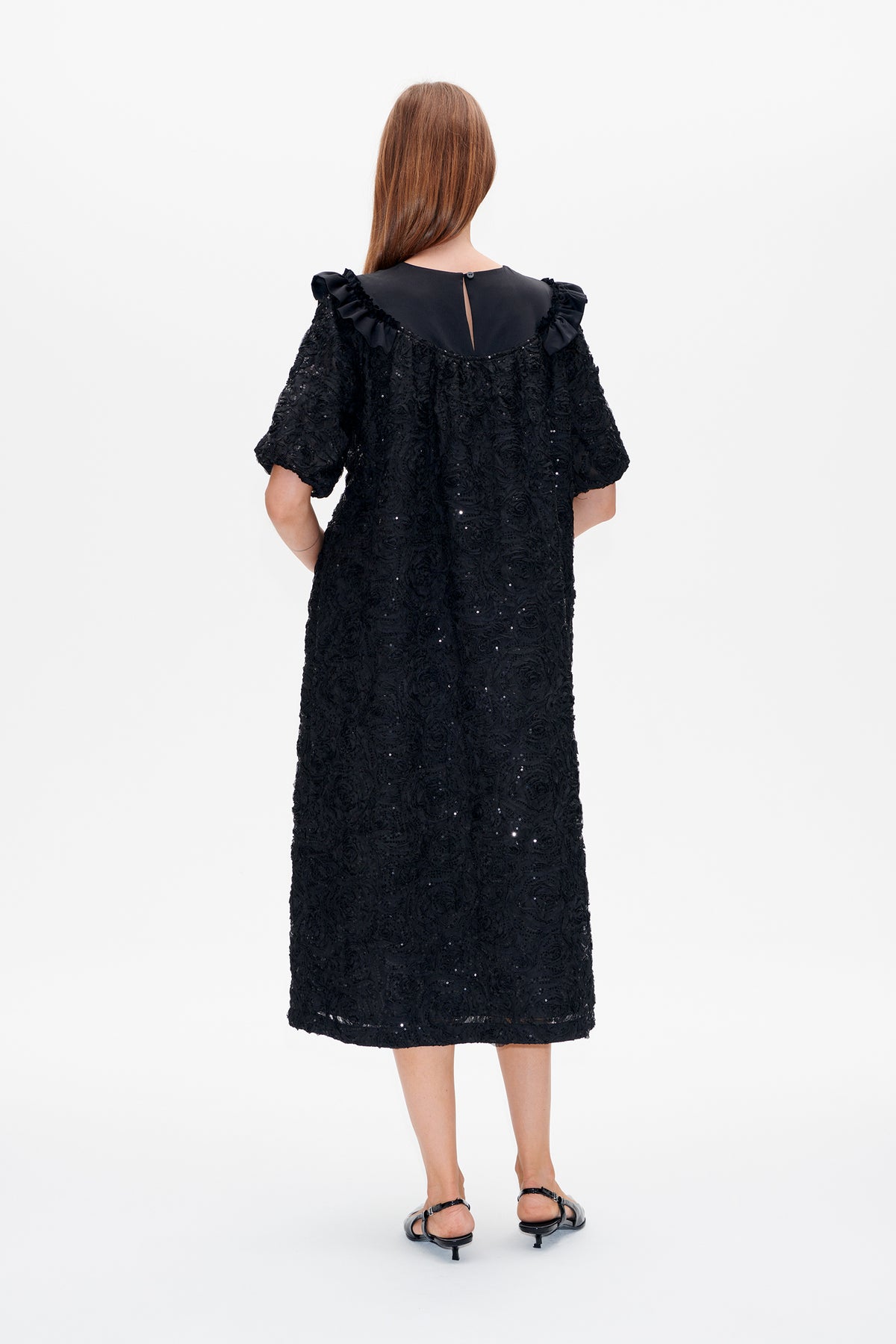 Back view of a black knee-length dress with short puff sleeves, ruffled neckline, and textured floral fabric dotted with sequins.