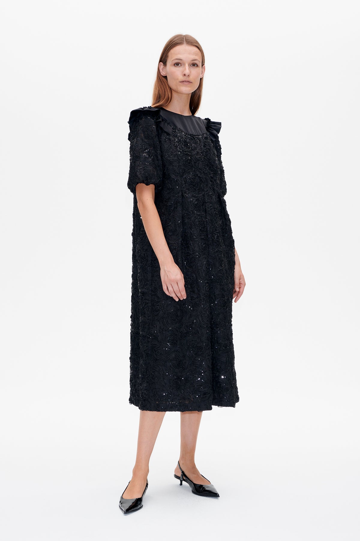 Front view of a black knee-length dress with textured floral detailing, scattered sequins, short puff sleeves and ruffled shoulders.