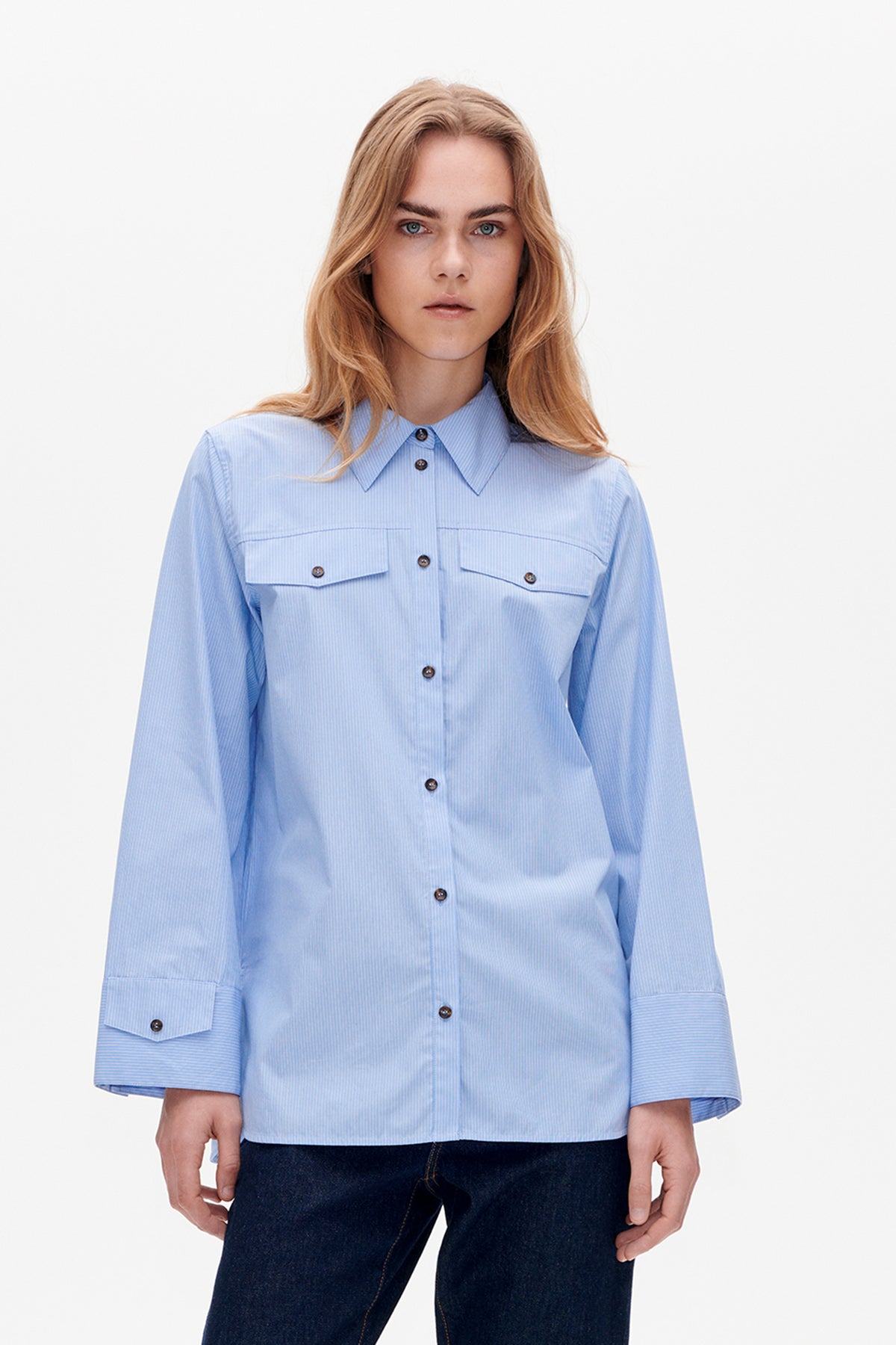 Vooraanzicht van een lichtblauwe, fijngestreepte blouse met knoopsluiting, puntkraag, borstzakken en ruime driekwartmouwen.