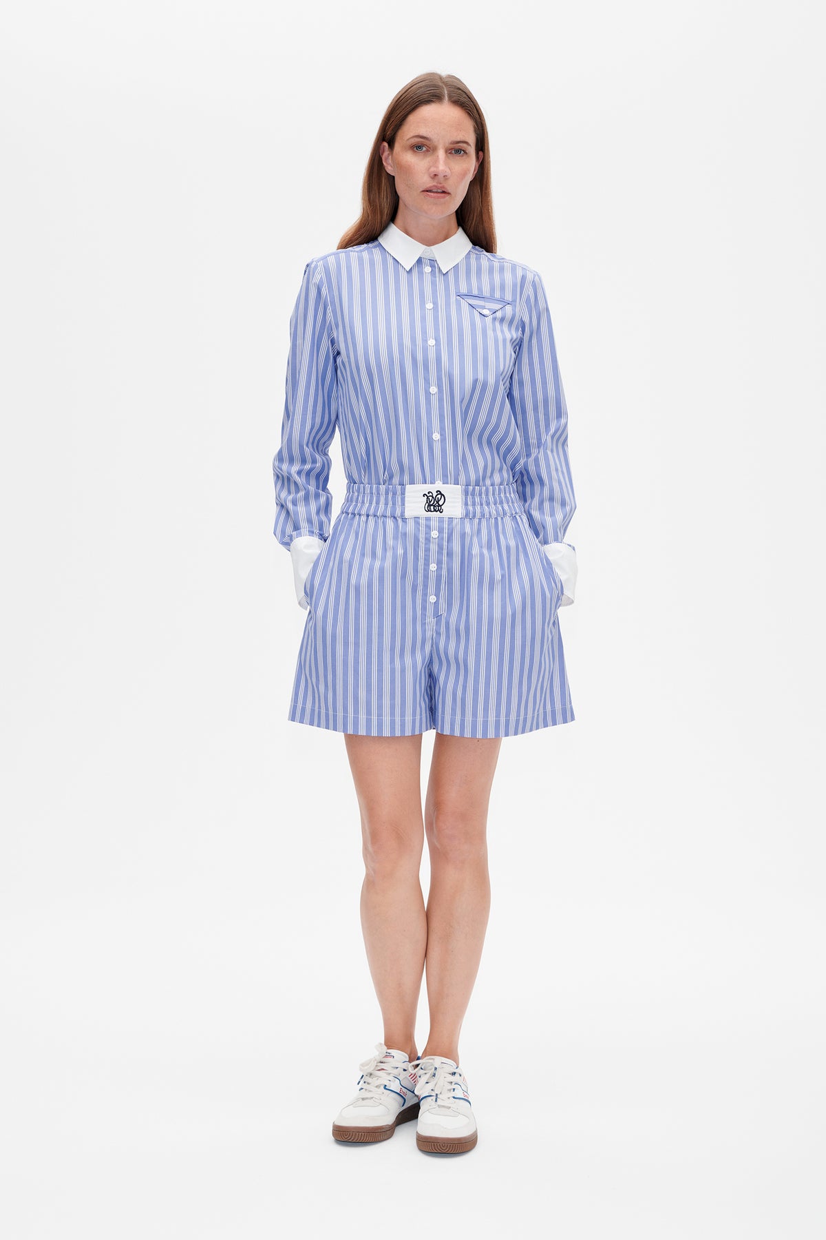 Model wearing a blue-and-white vertically striped button-up shirt with white collar and cuffs, paired with matching high-waisted shorts.