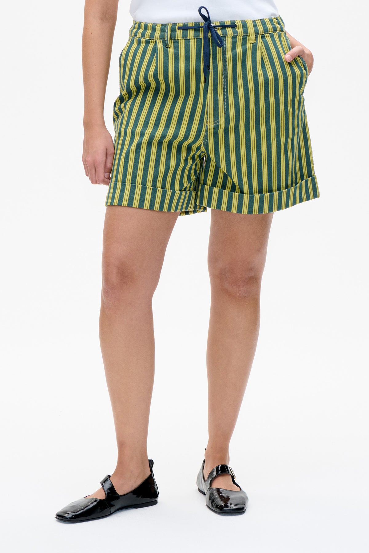 Front detail of green shorts with vertical yellow stripes, a navy drawstring waist, and large cuffed hems.