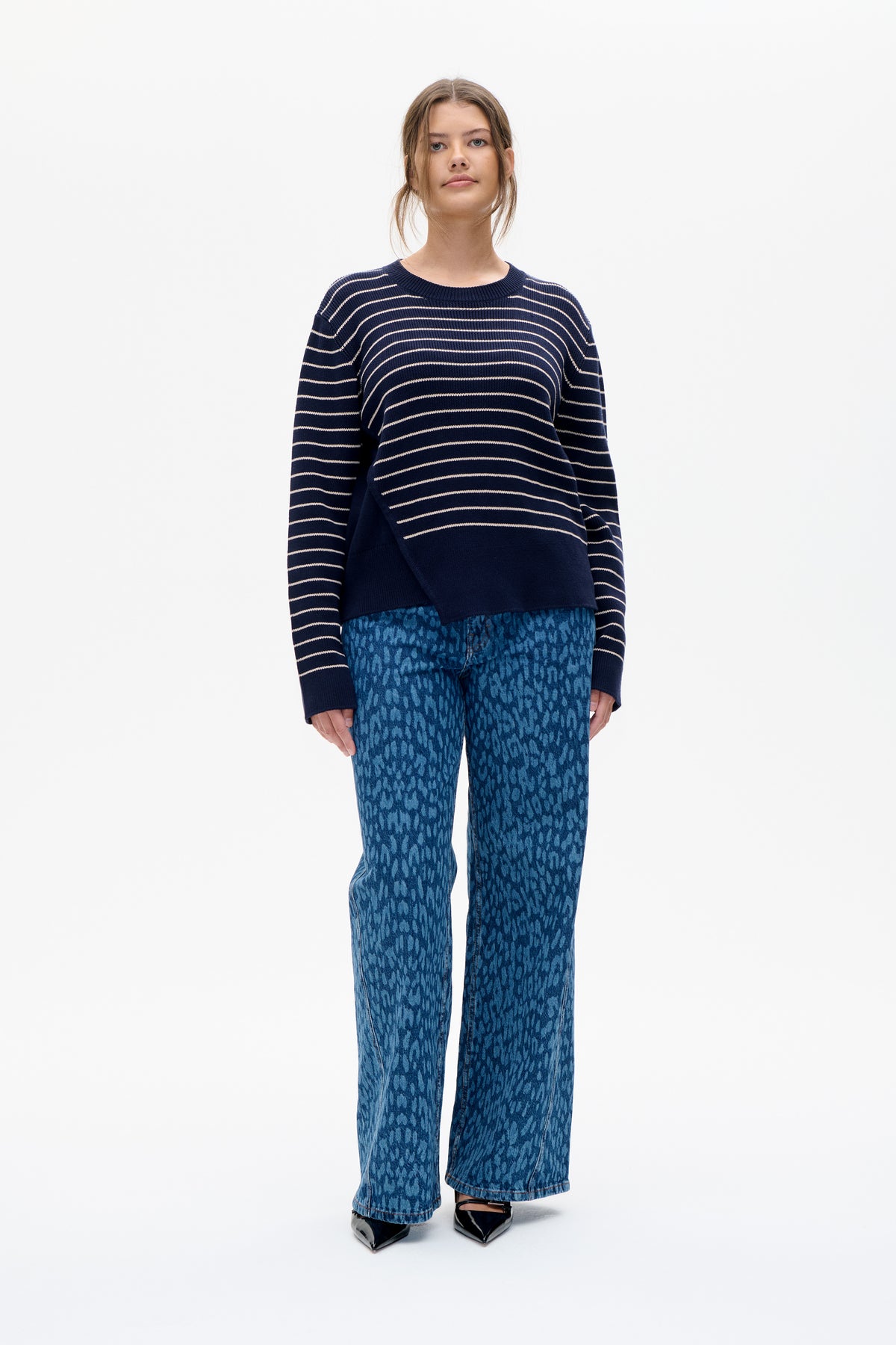 Front view of a model wearing a navy crew-neck sweater with thin cream stripes and blue patterned wide-leg jeans.