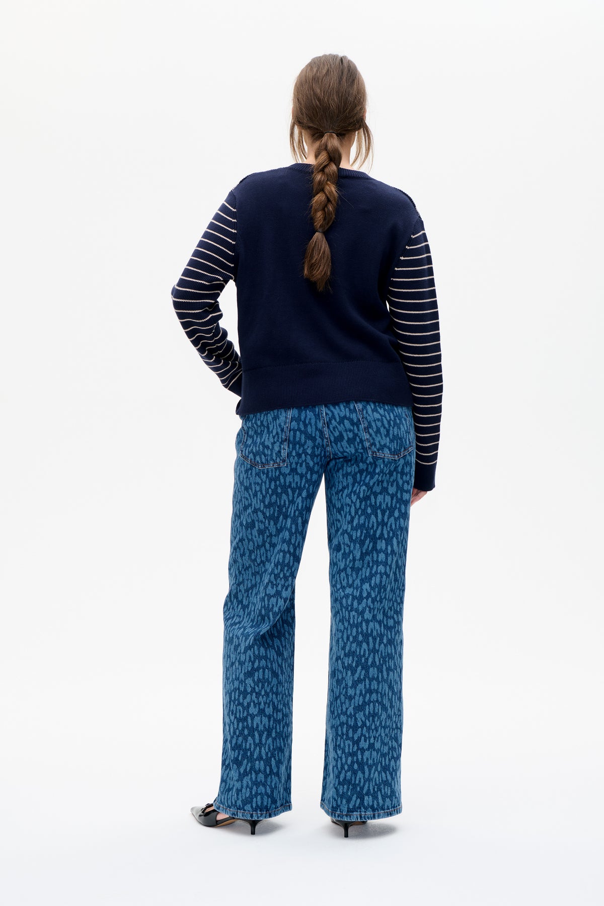 Rear view of a model wearing a navy knit sweater with cream striped sleeves and blue patterned wide-leg jeans.