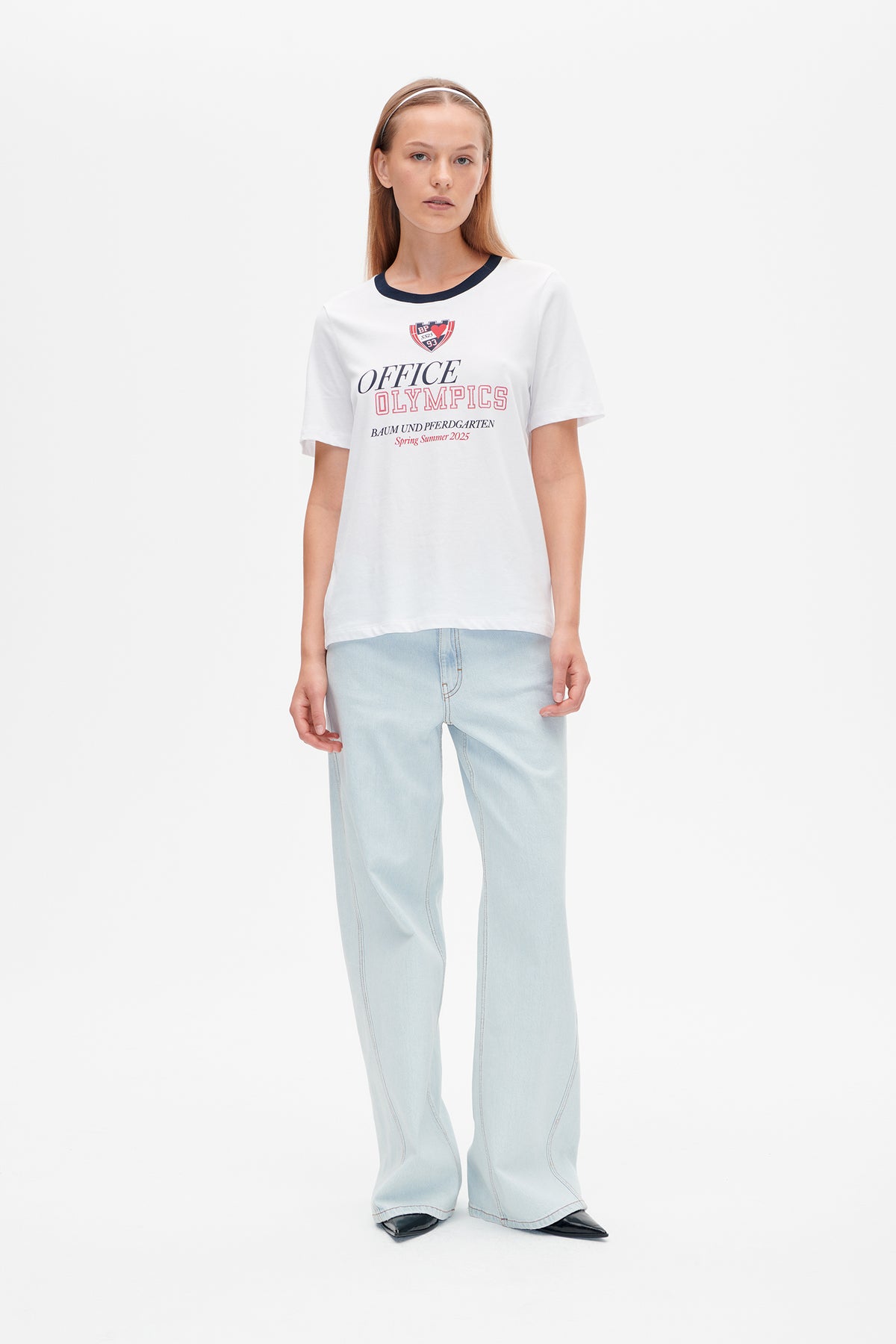 Mannequin portant un T-shirt blanc à manches courtes, col bleu marine et inscription rouge et bleu marine sur la poitrine, associé à un jean évasé bleu pâle.