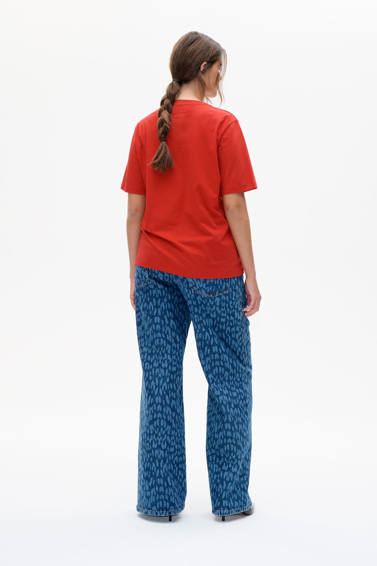 Back view of a model wearing a plain red short-sleeved T-shirt with blue patterned wide-leg jeans.