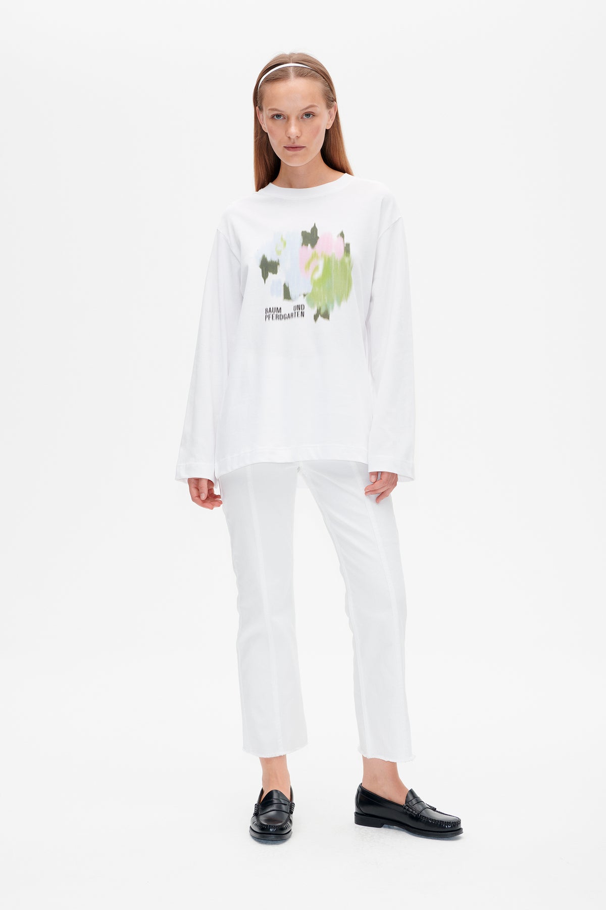 Front view of an oversized white long-sleeve top with a multicoloured abstract chest print and Baum und Pferdgarten lettering.