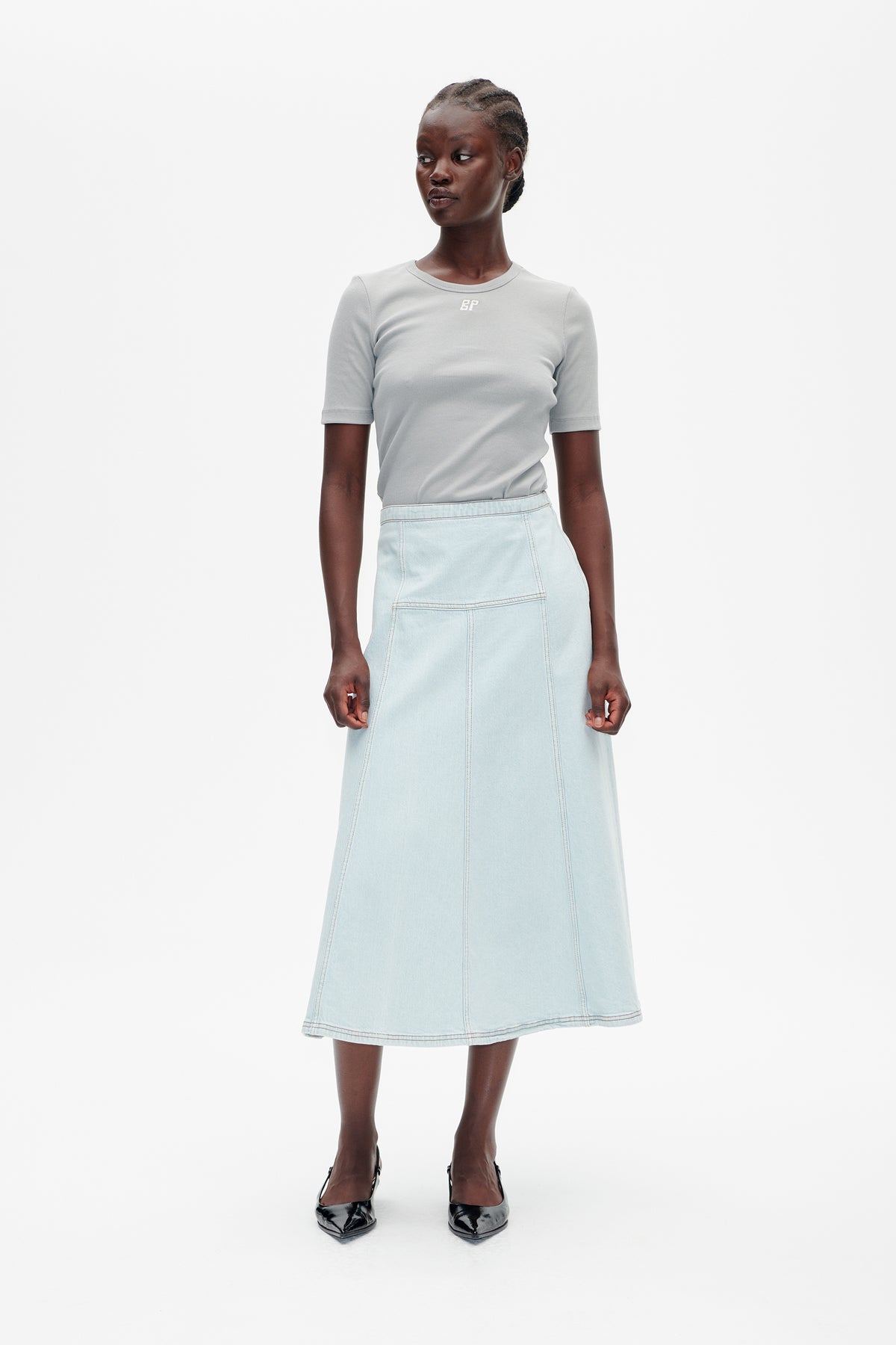 Front view of a model wearing a light grey short-sleeve T-shirt with a small chest logo and a pale blue panel-seamed midi skirt.