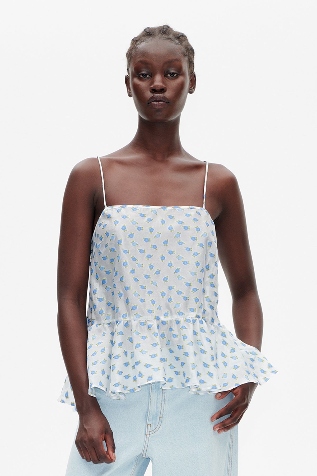 Front view of a white spaghetti-strap peplum top with a small blue floral print, styled with light-wash jeans.