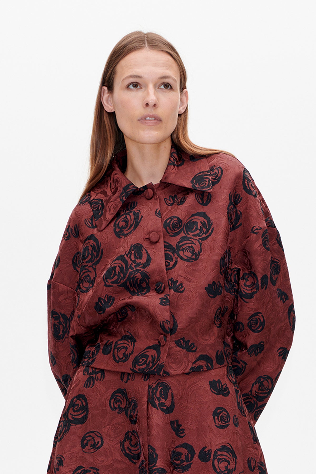 Close-up front view of a rust-red blouse with black abstract floral print, covered buttons and a wide folded collar