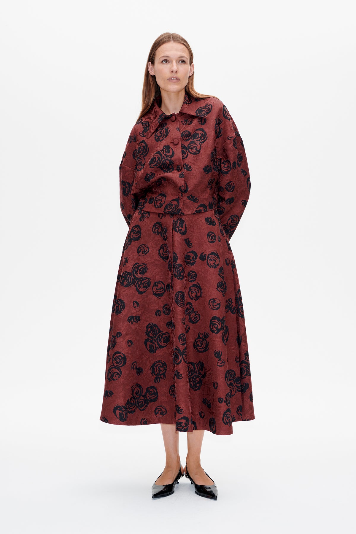Front view of a model wearing a burgundy button-front jacket and matching midi skirt with a black rose print.