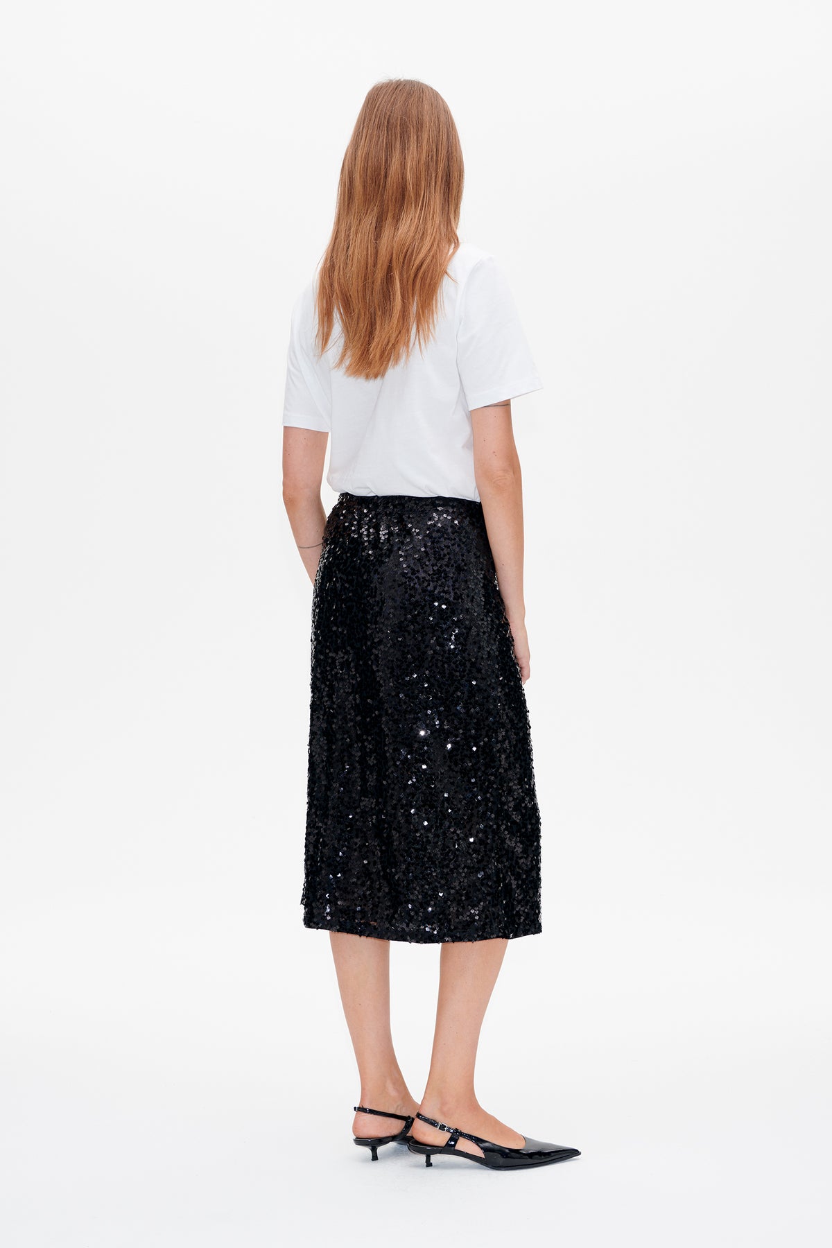 Back view of a model wearing a plain white short-sleeve T-shirt and a black sequin midi skirt.