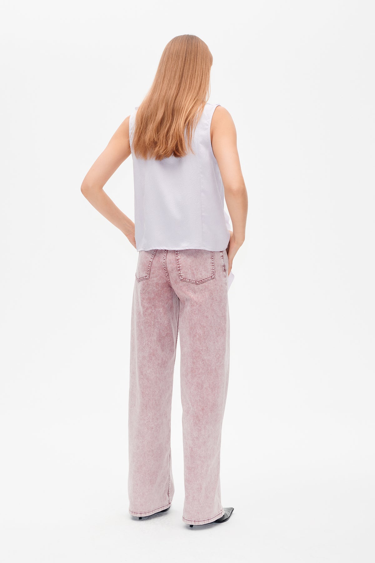 Back view of a model wearing a pale lavender sleeveless top with a subtle raised pattern and pink acid-wash wide-leg jeans.