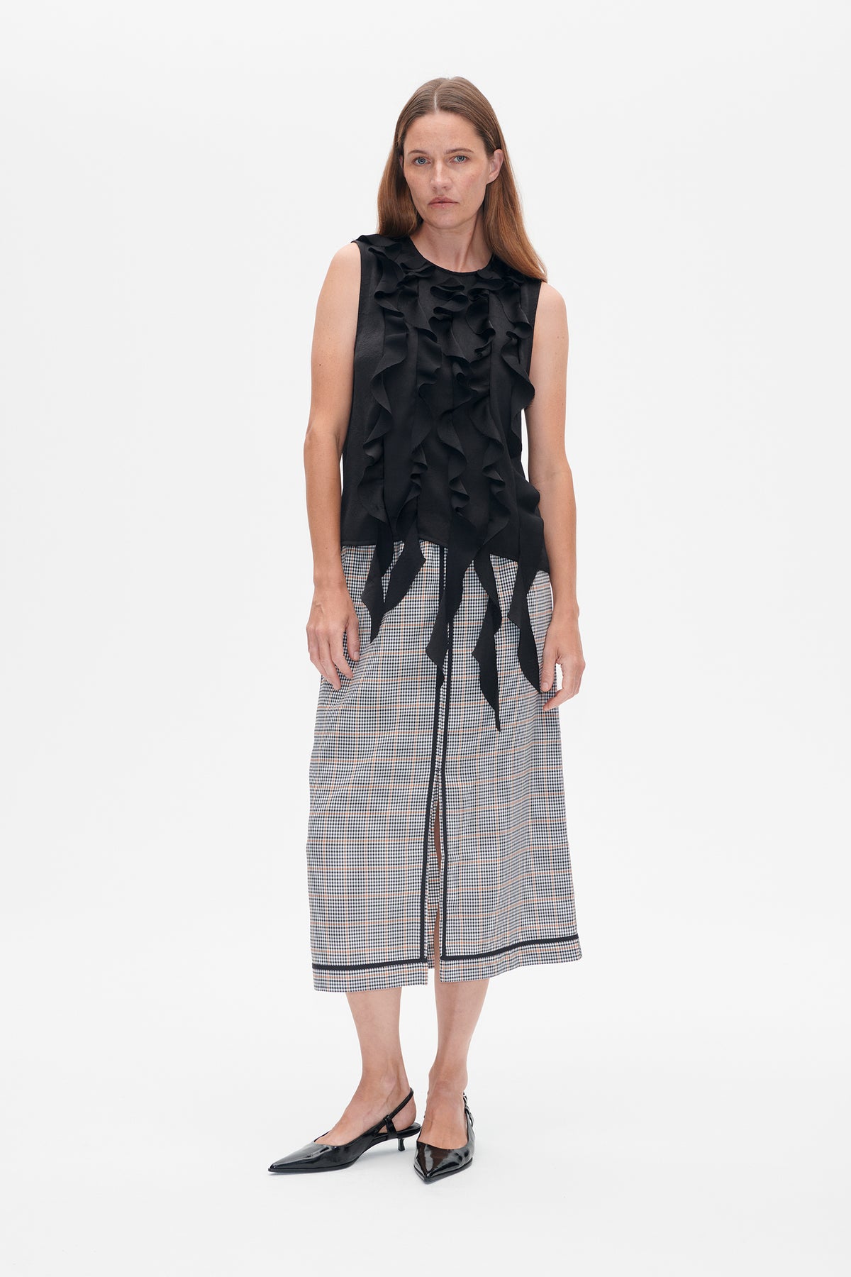 Front view of a model wearing a black sleeveless ruffle top with long ties and a checked midi skirt with black trim.