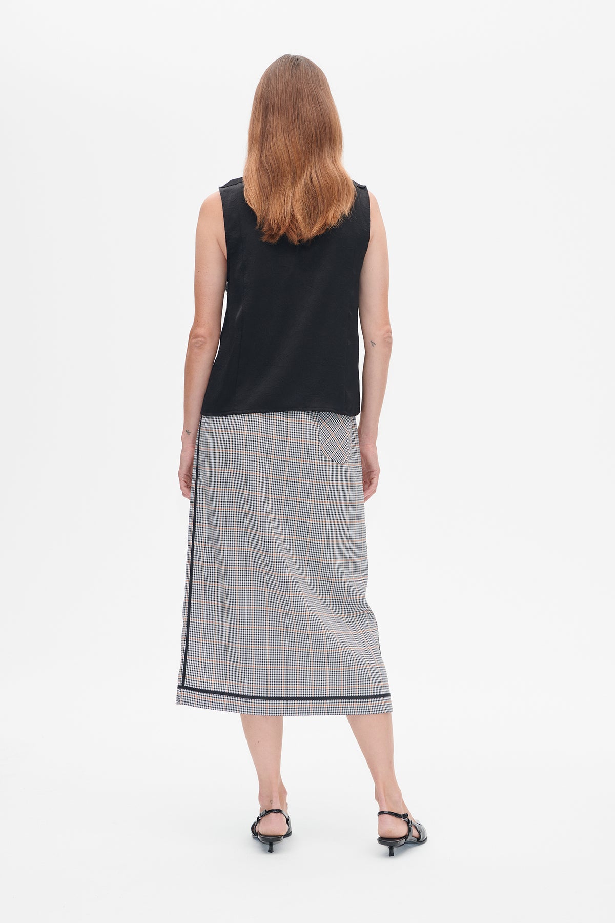 Back view of a model wearing a black sleeveless top and a checked midi skirt with black trim.