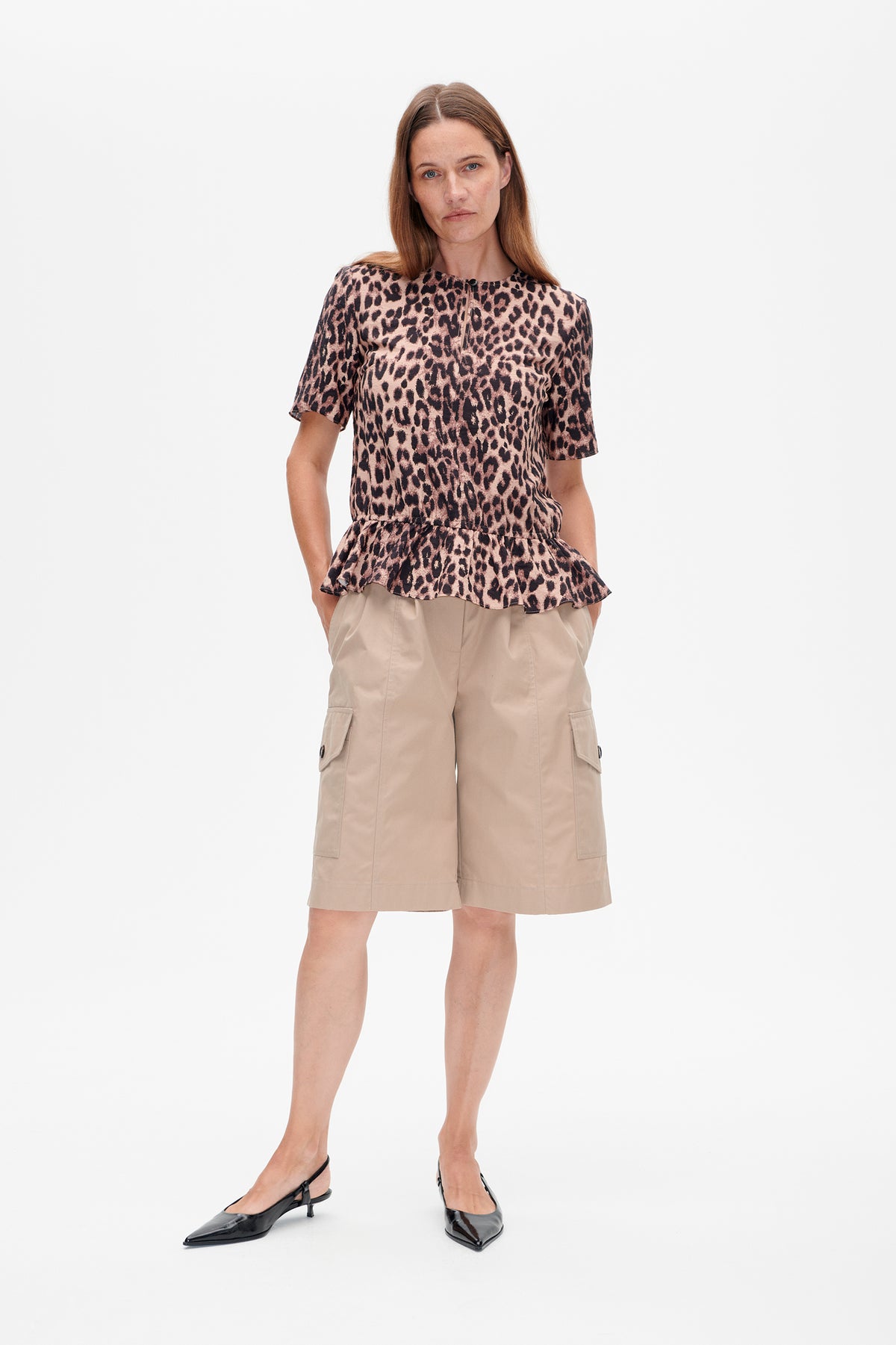 Vorderansicht eines Models, das ein kurzärmeliges rosa-braunes Top mit Leopardenmuster und ausgestelltem Peplum-Saum trägt.
