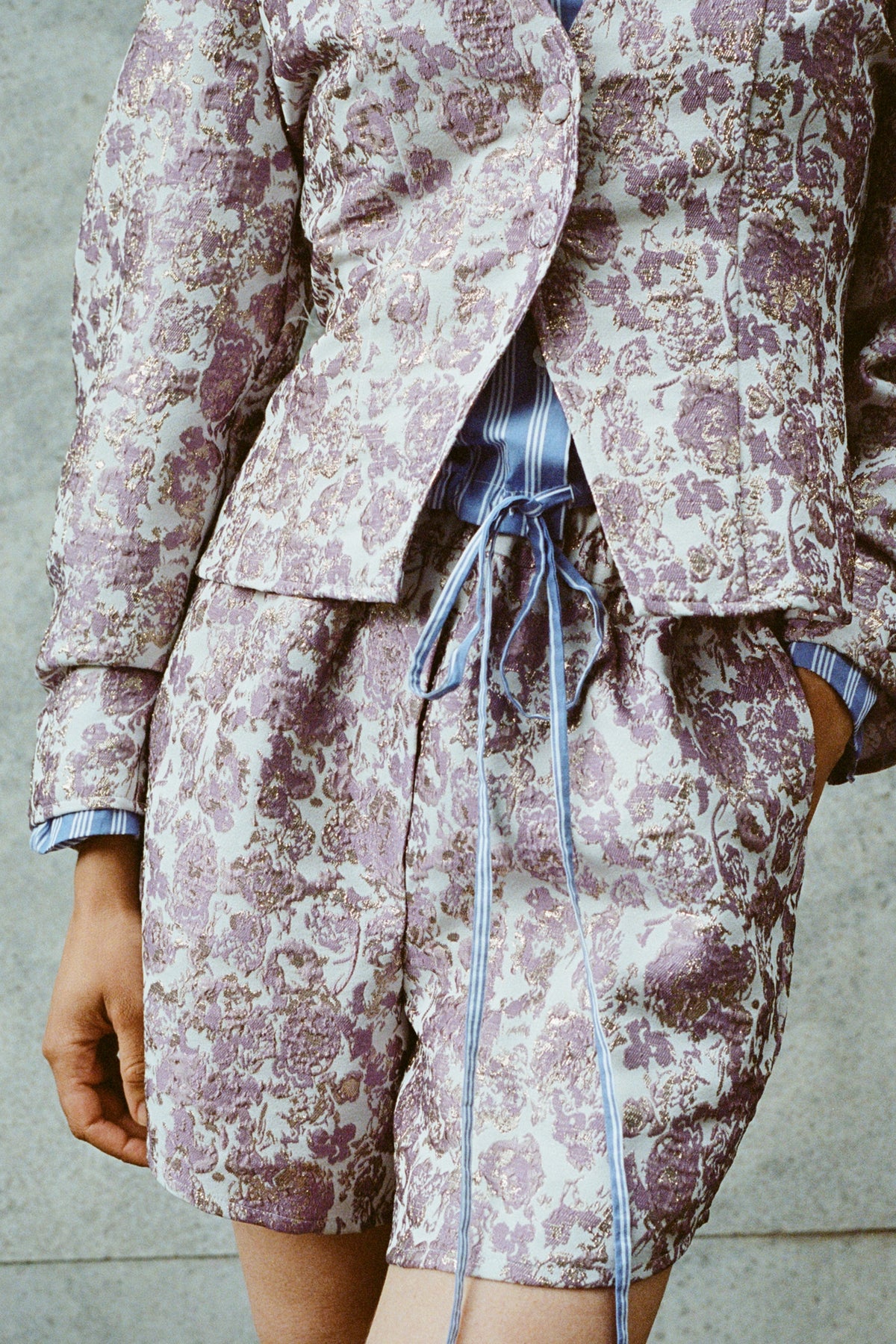 Close-up campaign view of a model wearing a cream and lilac patterned jacket over a blue striped top with long ties.