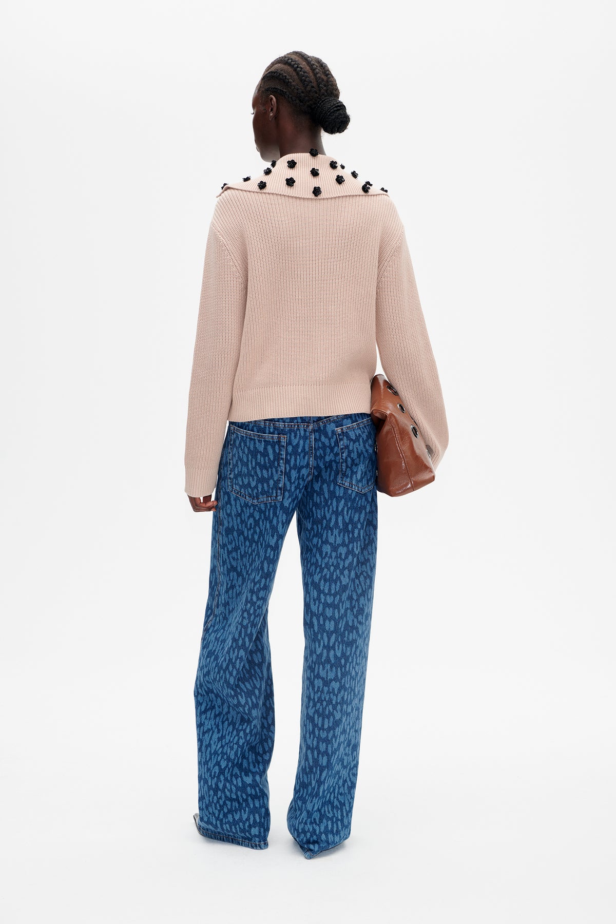 Back view of a pale pink knit sweater with a wide collar embellished with black flowers, paired with blue patterned jeans.