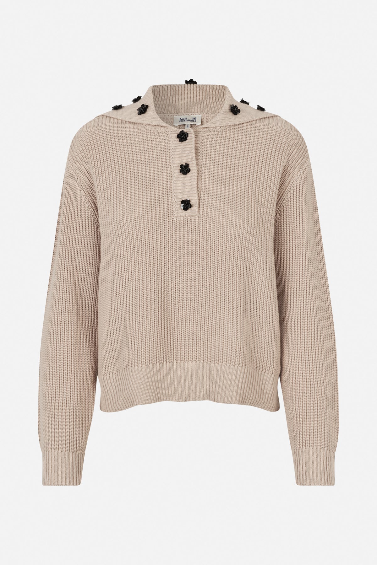 Front view of a beige ribbed knit sweater with a wide collar, black flower-shaped buttons and floral embellishments.