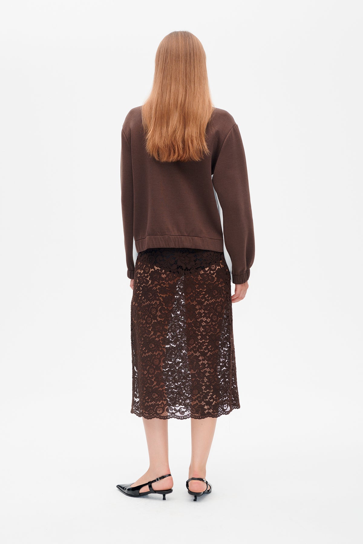 Back view of a model wearing a dark brown long-sleeved sweatshirt and a knee-length floral lace skirt with a scalloped hem.